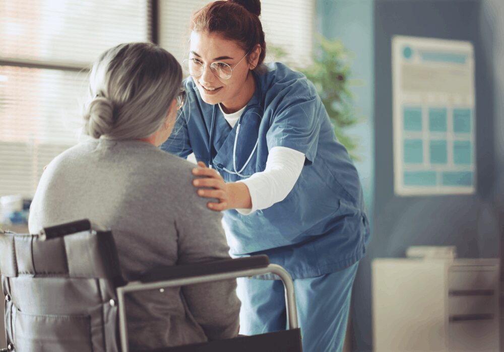 Nurse comforting elderly patient in wheelchair.