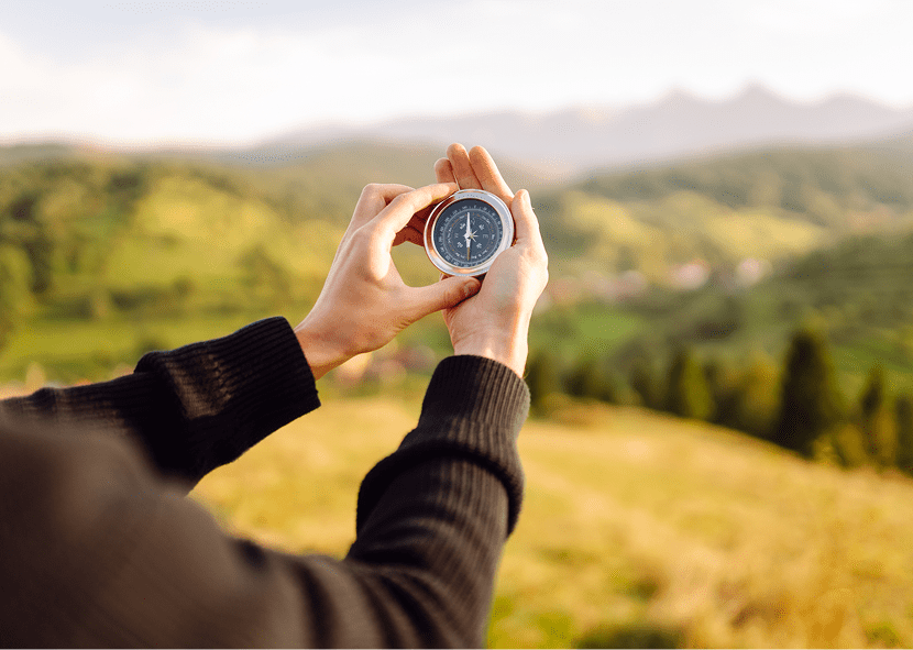 Hands holding compass in scenic landscape.