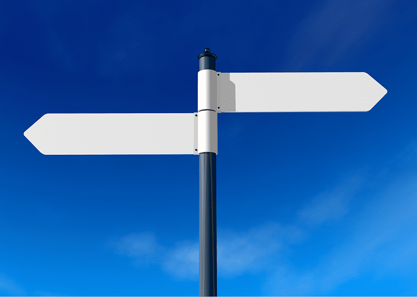 Blank directional signpost against blue sky.